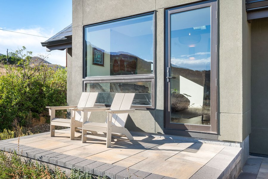 Two Adirondack chairs beside a tall window on the stone patio