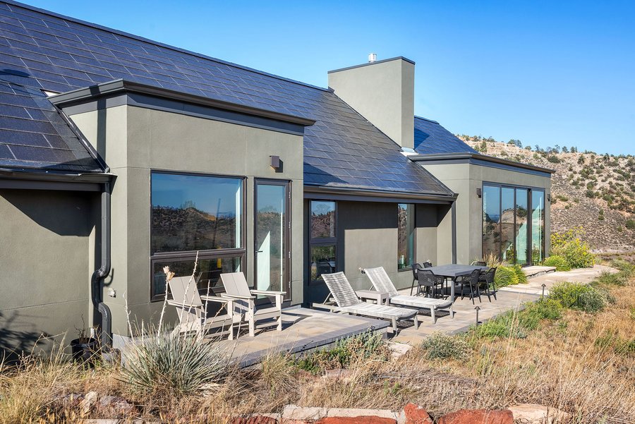 Rear patio with lounge chairs and a dining table beside floor-to-ceiling glass