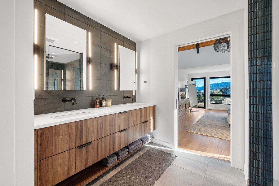Primary bath double vanity with lit mirrors, and the bedroom beyond