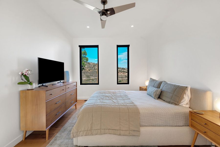 Bedroom with a king bed, TV on a wood dresser and two tall windows