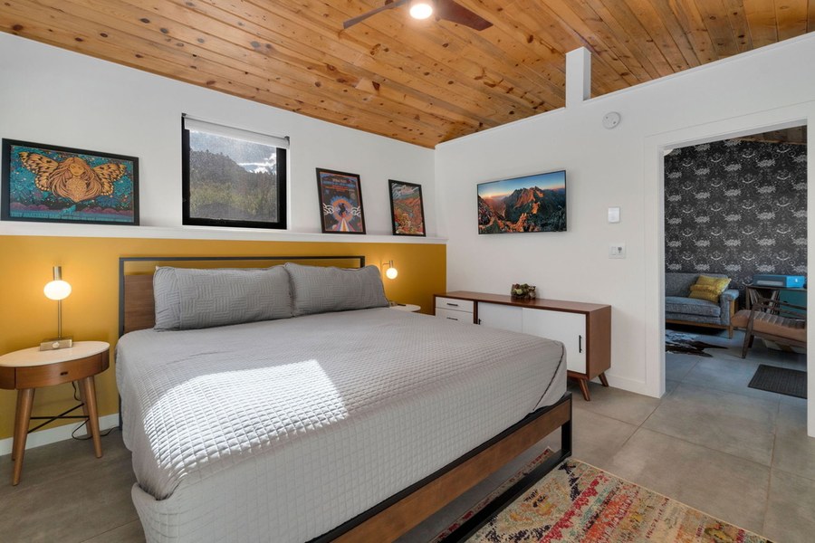 King bed with a wood ceiling and the living room beyond
