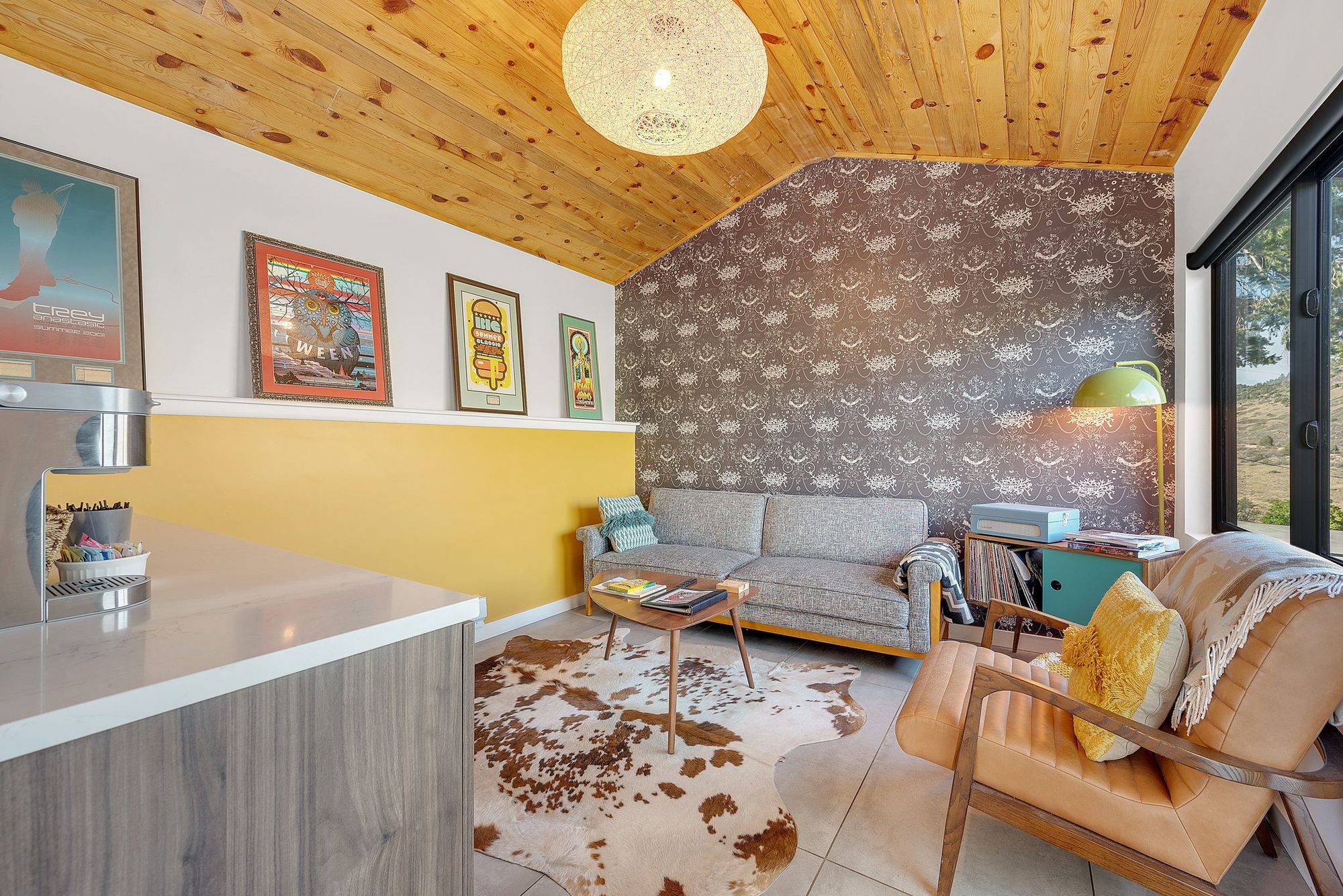 Guesthouse living room with a gray sofa, leather chair, framed posters and patterned wallpaper