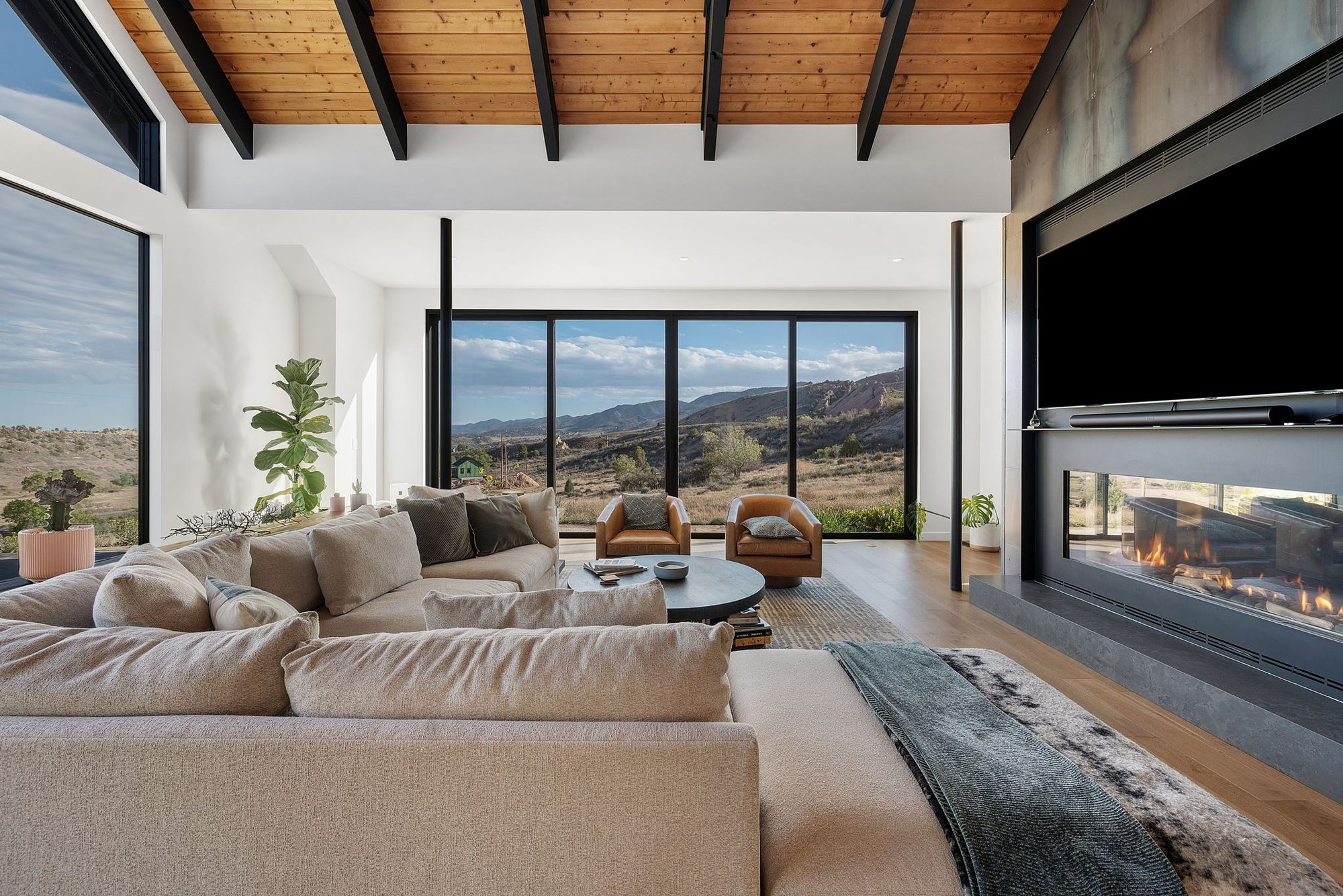 Great room seating facing a linear fireplace under a timber ceiling