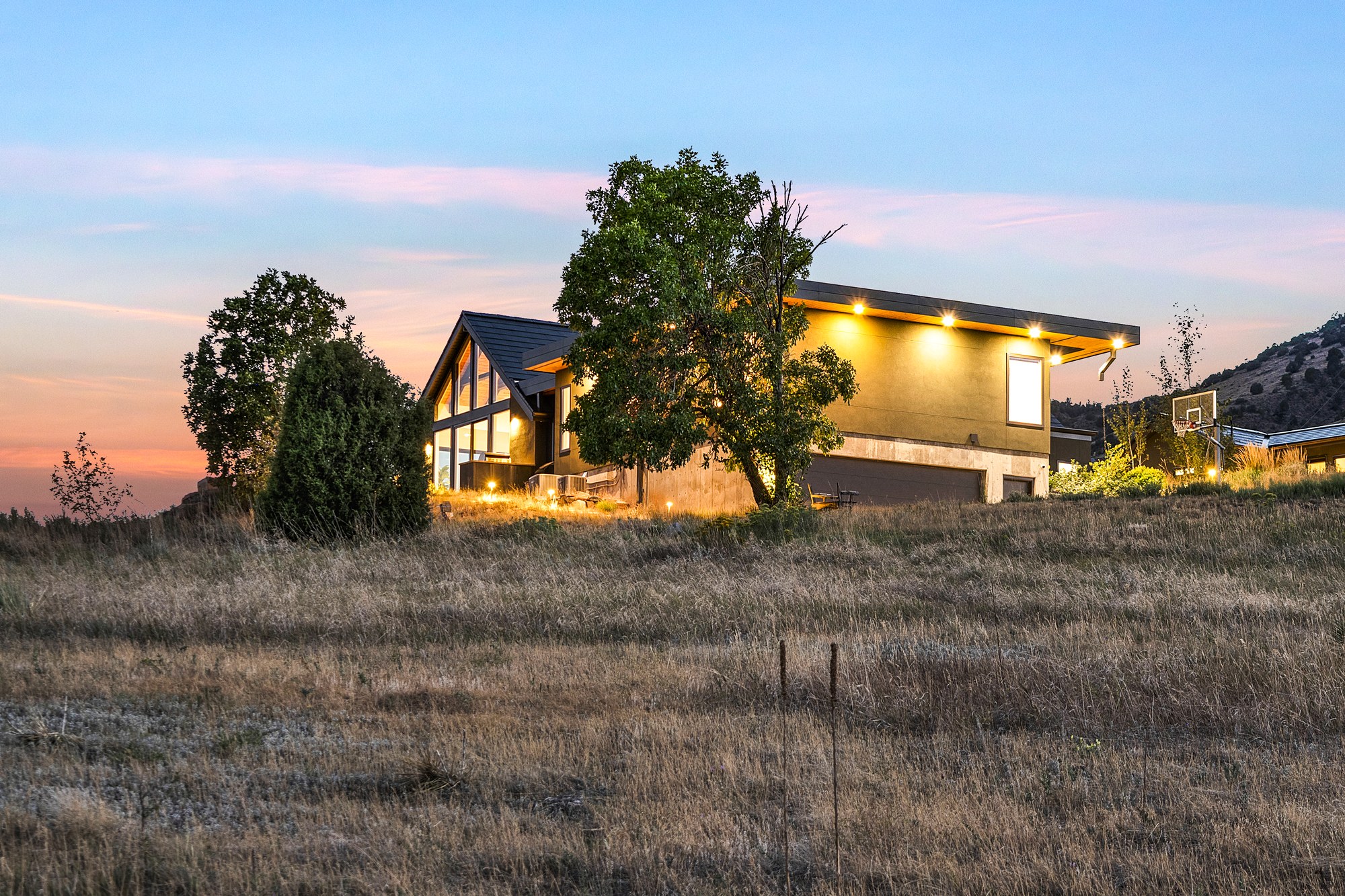 The house glowing at dusk, with lit windows and eaves under a pink and blue sky