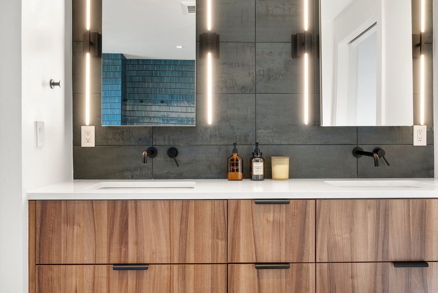 Primary bath double vanity with lit mirrors and walnut cabinetry