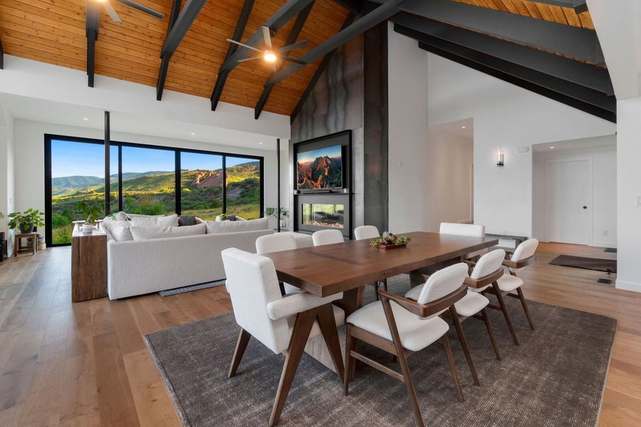 Dining table beside a double-sided fireplace, with the great room and mountain views beyond