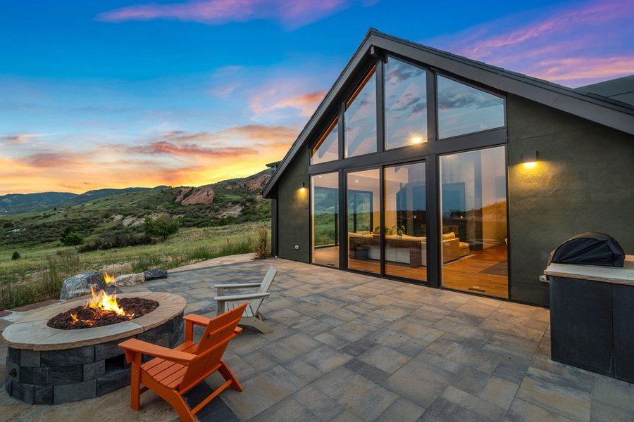 Fire pit and orange chair on the patio at sunset, with the glass gable of the main house glowing