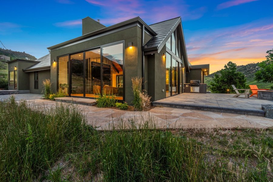 Rear of the main house at dusk, with the glass wall, lit sconces and outdoor kitchen