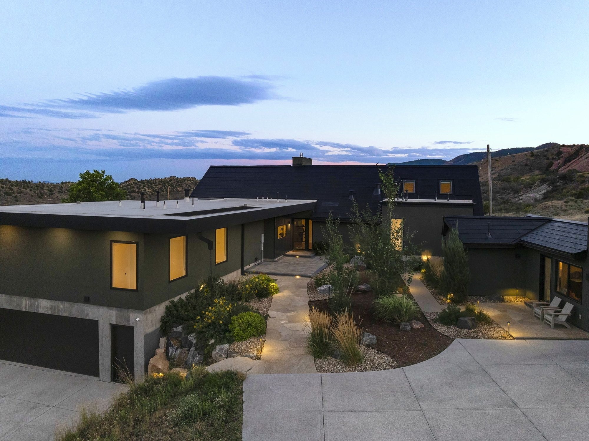 The main house at dusk, with lit windows, a stone path and mountains beyond